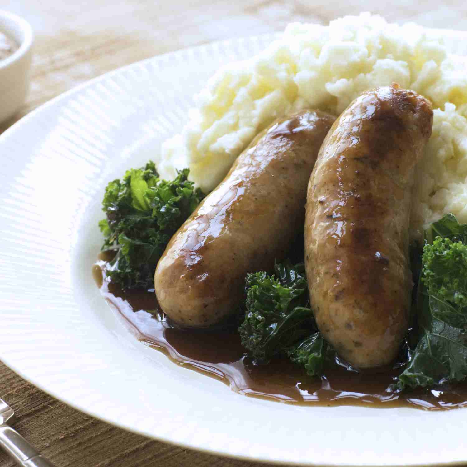 Showing two cooked sausages gluten-free on a plate, with mashed potatoes and gravy. 