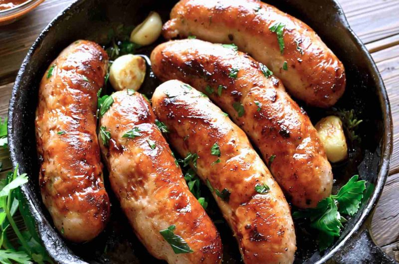 Gluten-free sausages in a black cast-iron casserole dish.