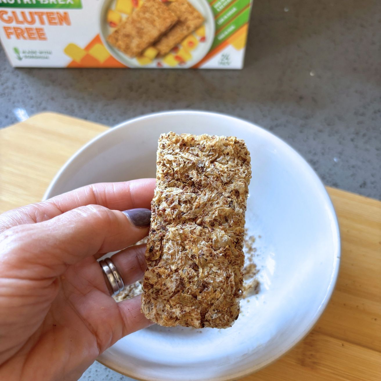 Hand holding one gluten-free weetabix made from sorghum showing close up texture of breakfast cereal
