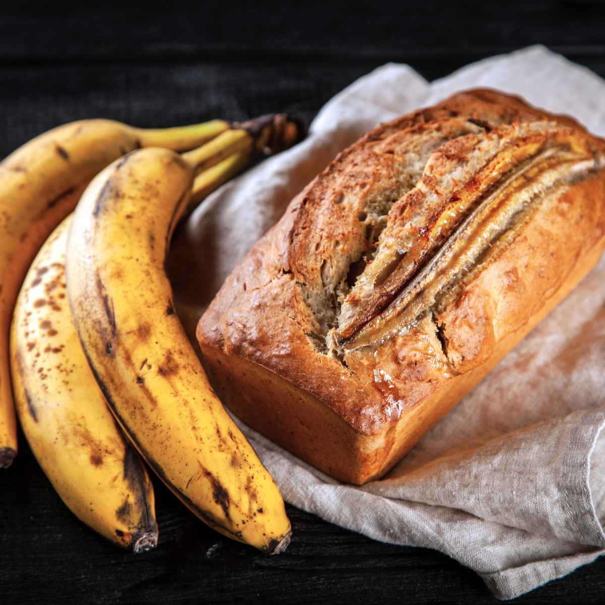 full loaf of gluten free banana bread with a few over-ripe bananas to the side.