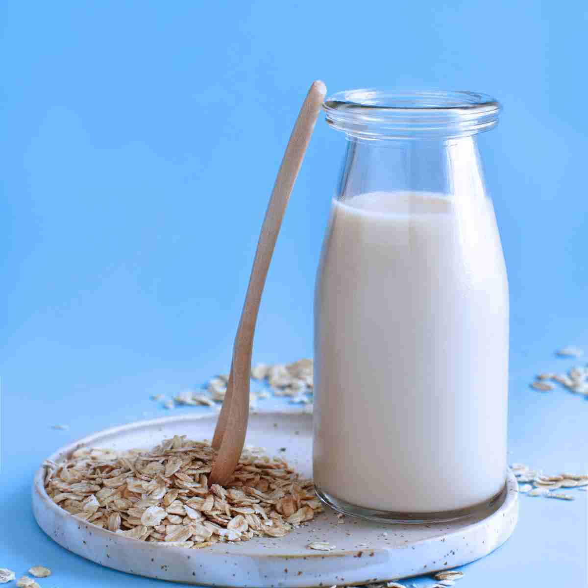 small glass of oat milk styled with wooden spoon and oat flakes.